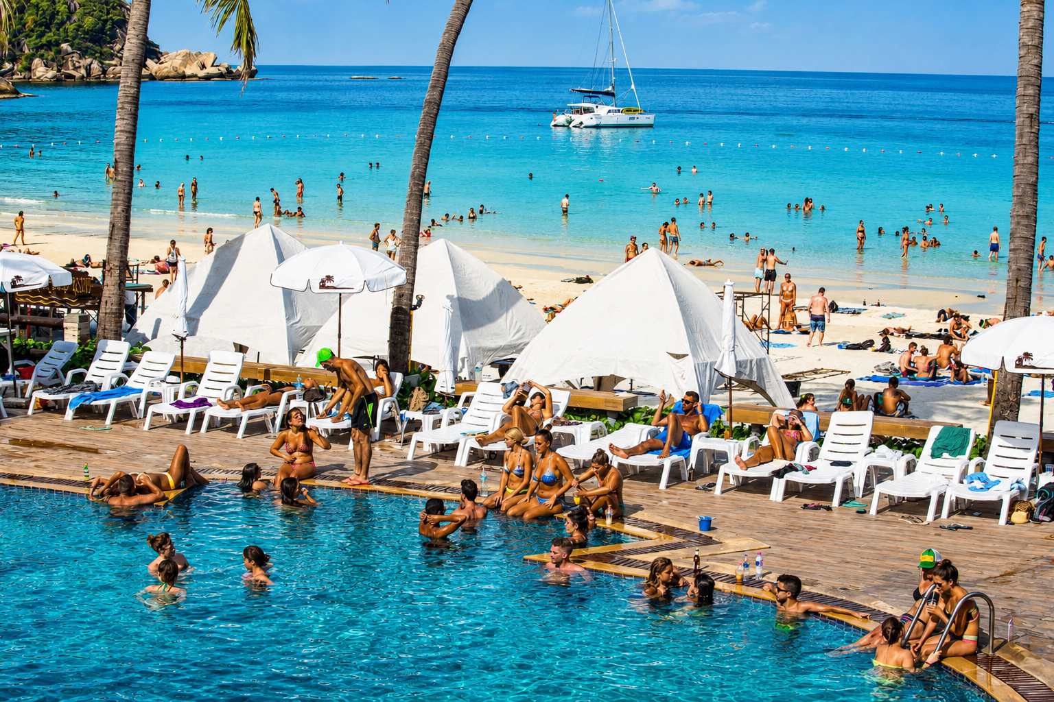 Busy beach resort pool and turquoise ocean showing how many people love to travel